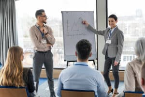 Business professionals giving presentation with graph on flip chart to audience