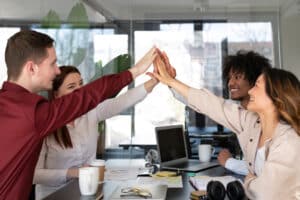 Diverse team of young professionals giving high five during meeting in modern office