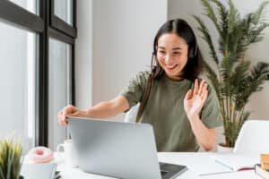 Smiling woman wearing headset waving during video call on laptop