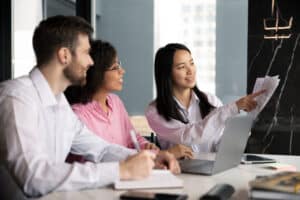 Three colleagues in business meeting reviewing documents and laptop screen