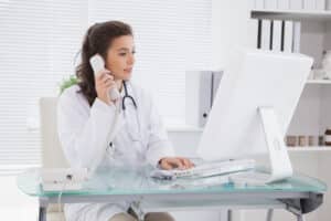 what do medical receptionist do Female doctor in white coat using computer and phone