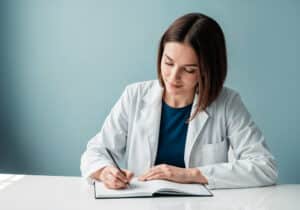what is a medical scribe Female doctor in white coat writing notes in notebook at desk