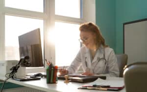 what is an er scribe Doctor writing patient notes at desk in sunlit medical office.