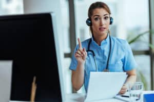 A healthcare professional with a headset and stethoscope engages in an online consultation