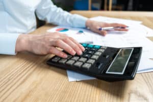 Close-up of person using calculator with financial documents and charts on wooden desk