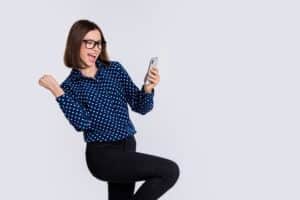Excited young woman celebrating while looking at smartphone