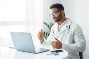 Male doctor with stethoscope providing telemedicine consultation on laptop