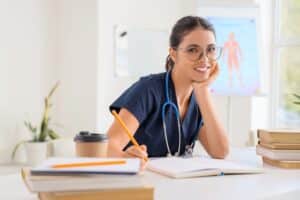 Smiling female medical professional in scrubs studying with notebook