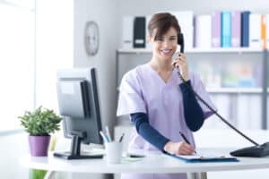 Smiling nurse in scrubs talking on phone while writing
