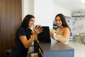 Smiling receptionist assisting young woman with digital check-in at clinic front desk