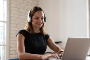 Smiling woman wearing headphones working on laptop during online