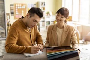 A designer takes notes while collaborating, showing support from medical scribe solutions.