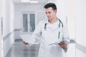 A doctor reviews medical documents in a hospital hallway, assisted by a doctors scribe