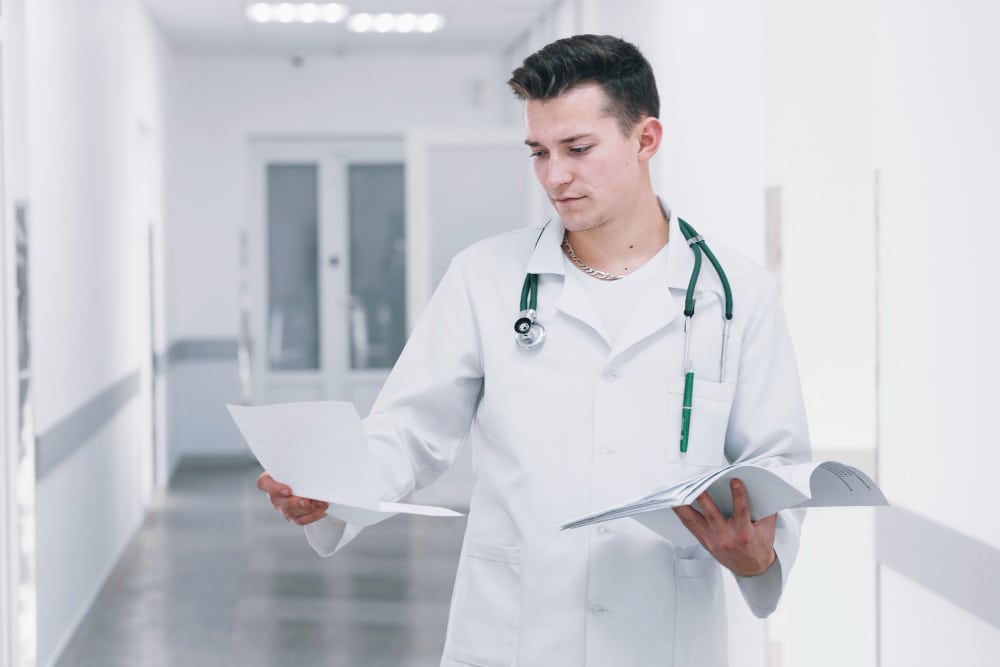 A doctor reviews medical documents in a hospital hallway, assisted by a doctors scribe