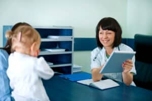 A pediatrician smiles while reviewing notes in the Speech Therapy Coding Handbook