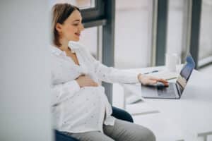 A pregnant woman works on a laptop, representing prenatal healthcare billing