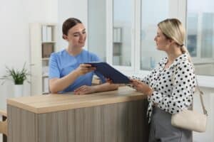 Definition of Receptionist handing a clipboard to a smiling visitor at a modern medical office front desk