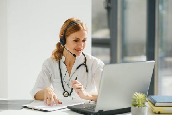 Female doctor with headset providing virtual patient consultation via laptop