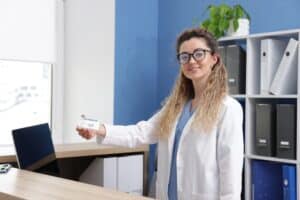 Friendly medical receptionist handing a card to a patient at a modern clinic front desk