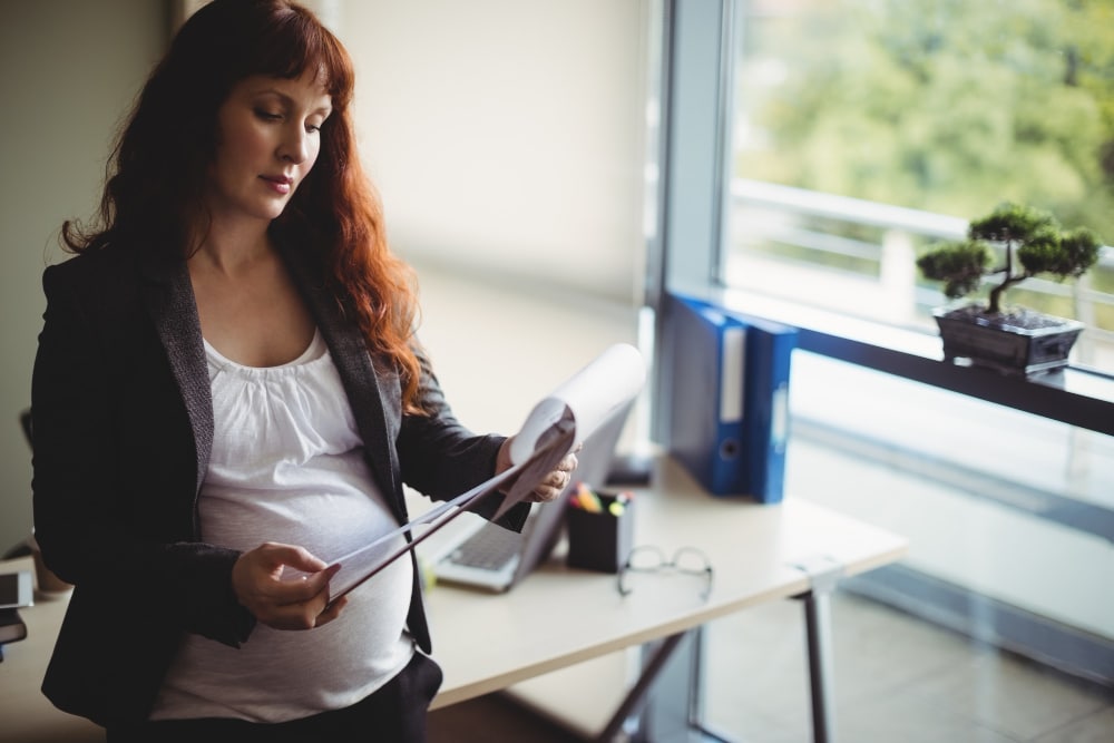 Pregnant woman in office reading papers on maternity obstetrical care medical billing