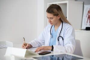 medical scribing by a female doctor in a white coat at a clinic desk