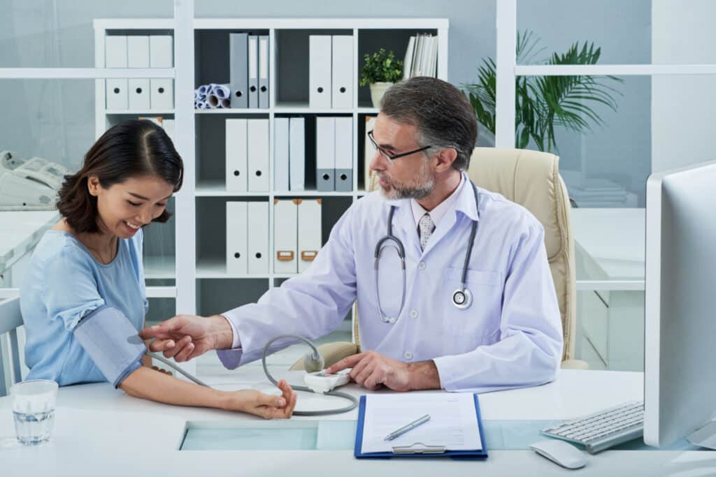 Doctor checking a female patient’s blood pressure during a post-discharge escalation workflow in a specialty clinic.