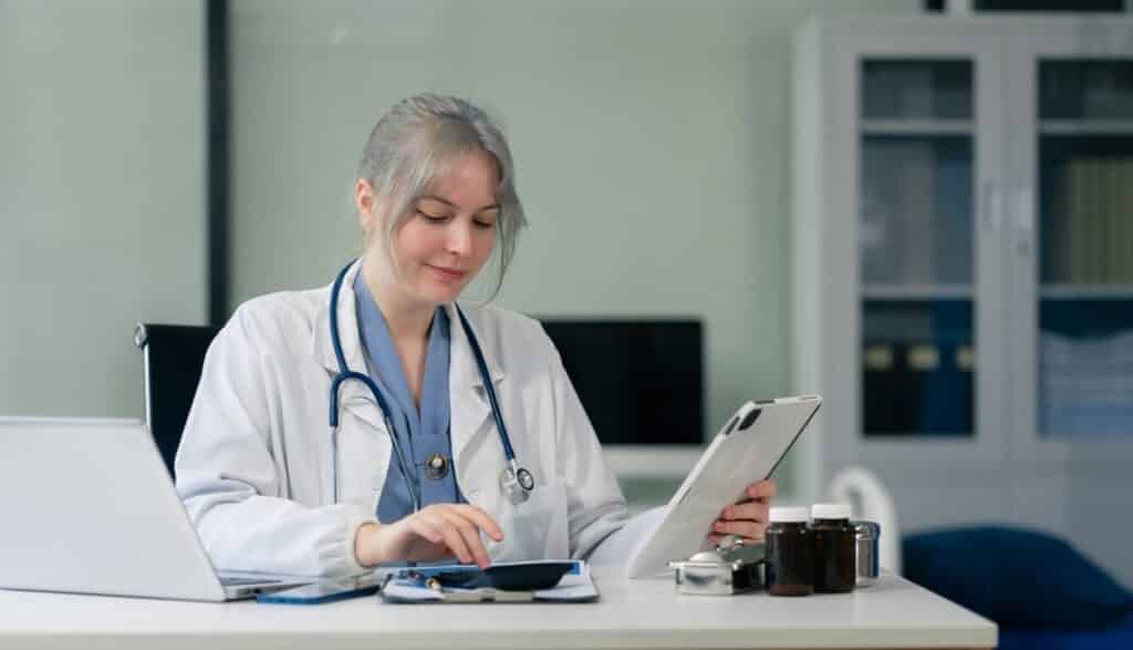 Doctor writing notes while using a calculator, virtual business support ROI model for healthcare admin overload in a clinic.