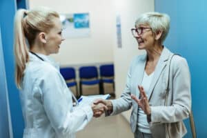 Happy senior woman shaking hands with a doctor while discussing care in a hospital hallway, specialty clinic referral follow-up workflow concept.