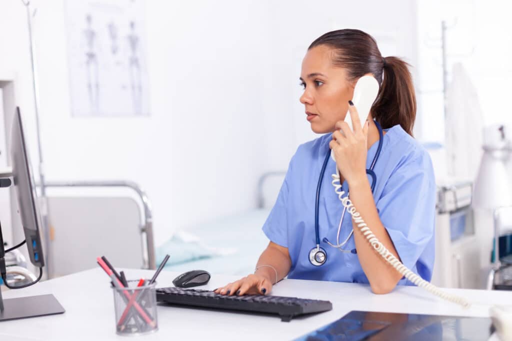 Nurse working at a clinic managing patient calls using telephone triage workflows that lower repeat urgent call volume.
