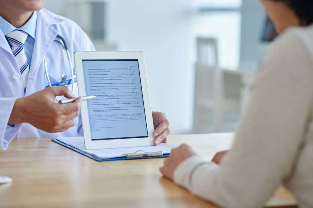 Prior authorization communication workflows doctor reviewing a digital tablet with a patient during a healthcare consultation.