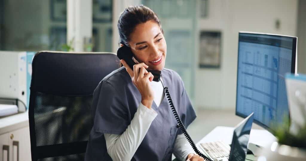 Telehealth Appointment Confirmation Workflow, doctor smiling while confirming an appointment via phone in a hospital.