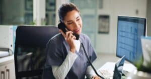 Telehealth Appointment Confirmation Workflow, doctor smiling while confirming an appointment via phone in a hospital.