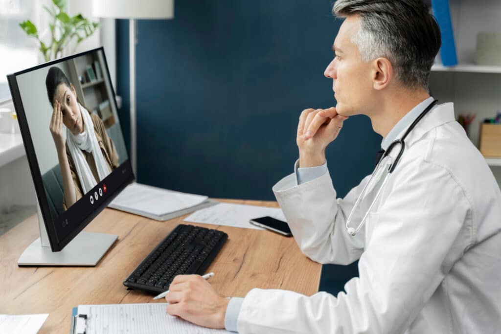 Telehealth appointment confirmation scripts displayed while a doctor conducts a video call consultation with a patient on a computer.