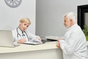 Virtual front desk workflow with a medical receptionist at a clinic front desk assisting an elderly man with patient check-in and support.