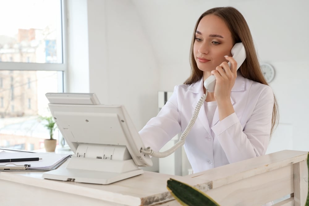 Female healthcare receptionist speaking on the phone while working at a clinic front desk