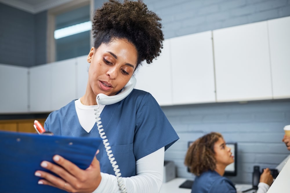 Female medical professional taking notes and using a smartphone while working in a healthcare setting
