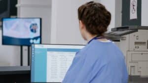 Medical nurse checking patient exam appointments on a computer at a hospital reception desk