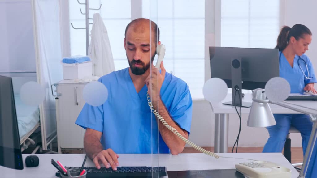 Nurse in a hospital clinic answering a phone call as part of a patient access follow-up calling workflow.