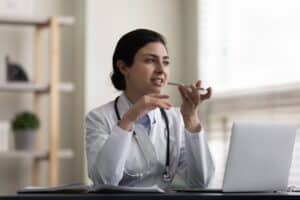Serious Indian female doctor recording an audio message on a smartphone, communicating with patients and supporting virtual healthcare conversations.