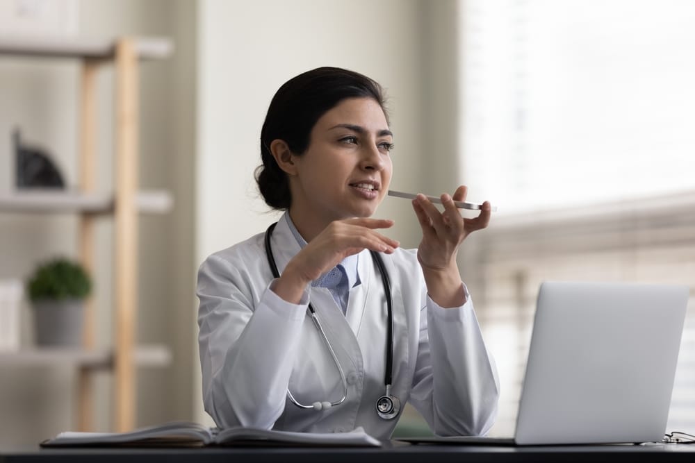 Serious Indian female doctor recording an audio message on a smartphone, communicating with patients and supporting virtual healthcare conversations.