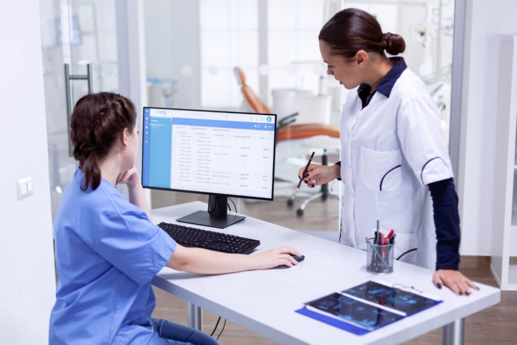 Two nurses in a clinic working on a computer while managing the patient acquisition workflow for medical practices.