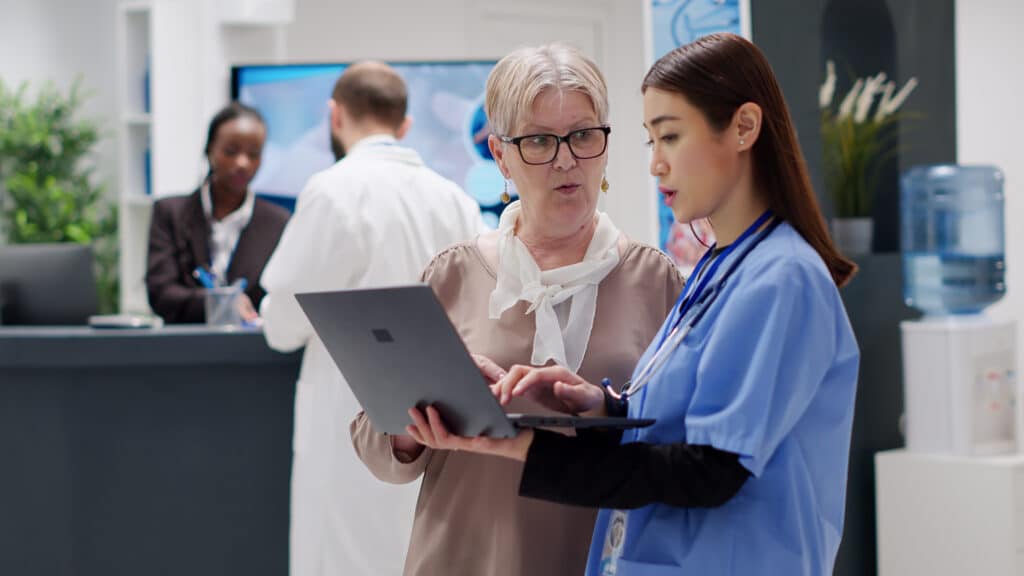 Senior woman and medical assistant analyzing a diagnosis report on a laptop during a healthcare consultation