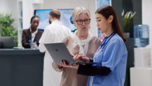 Senior woman and medical assistant analyzing a diagnosis report on a laptop during a healthcare consultation