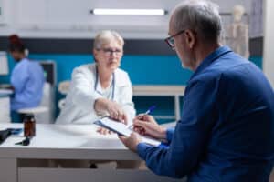 Senior patient signing appointment papers for doctor referral, specialist referral intake response standard.