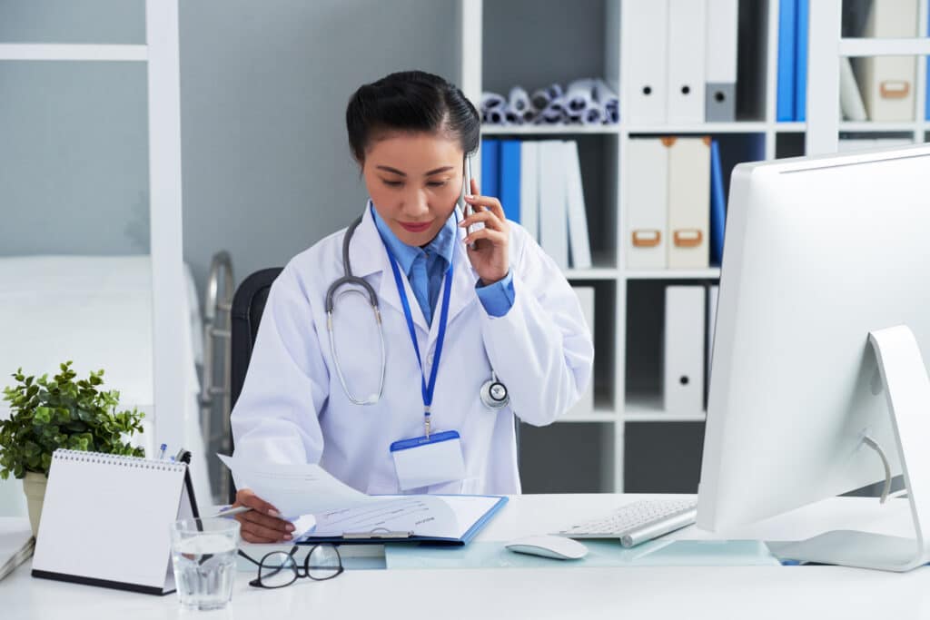 asian female doctor sitting desk office calling mobile phone