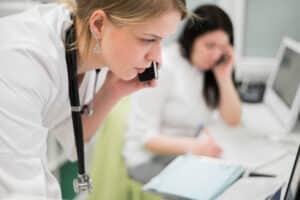 Doctor talking on the phone during a pre-visit insurance verification call quality control process.